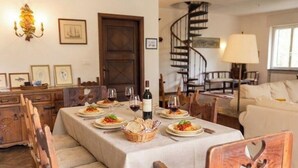 Ein Essbereich mit Tisch, gedeckten Plätzen, Stühlen, einer Chandelüster, einer Treppe und einem Sofa.