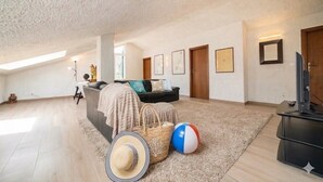 Ein geräumiges Wohnzimmer mit hoher Decke, einer Couch, einem Fernseher und einem Strandball.