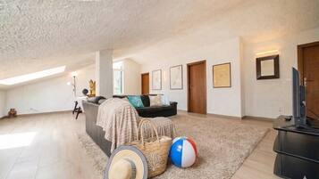 A spacious living room with a high ceiling, a sofa, a television, and a beach ball.