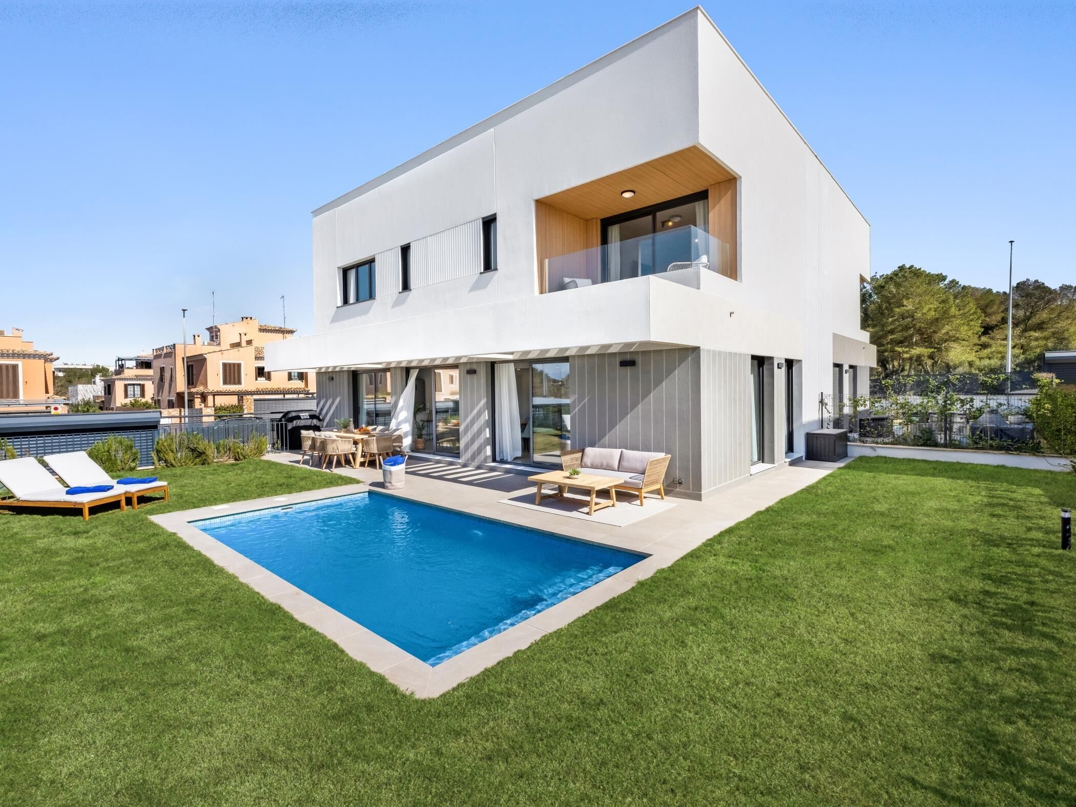 Una casa moderna de dos pisos con piscina, mobiliario exterior y césped bien cuidado.