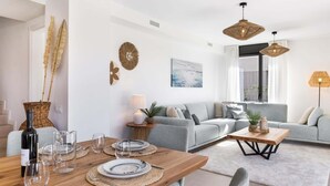 A modern living room with a grey sofa, a wooden dining table set with plates and glasses, and a large window with curtains. - Villa Oronella with Saltwater Pool, Premium Comfort & Elegant Design (Puigderros (Llucmajor))