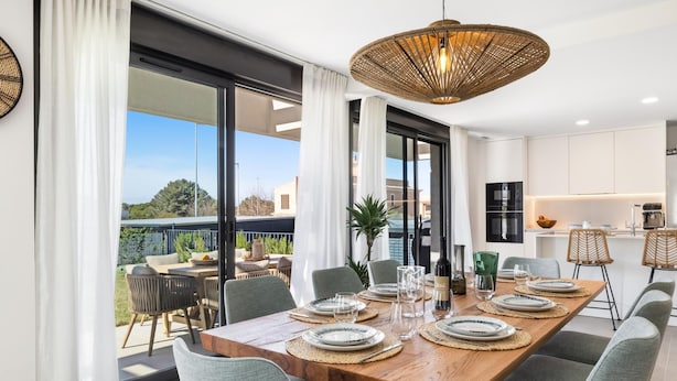 A dining area with a wooden table set for six, surrounded by grey upholstered chairs. A woven pendant light hangs above, and the room features large windows with white curtains. - Villa Oronella with Saltwater Pool, Premium Comfort & Elegant Design (Puigderros (Llucmajor))