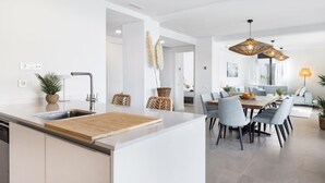 A modern kitchen with a central island, dining area with light blue chairs, and a living room with a sofa and a lamp. - Villa Oronella with Saltwater Pool, Premium Comfort & Elegant Design (Puigderros (Llucmajor))