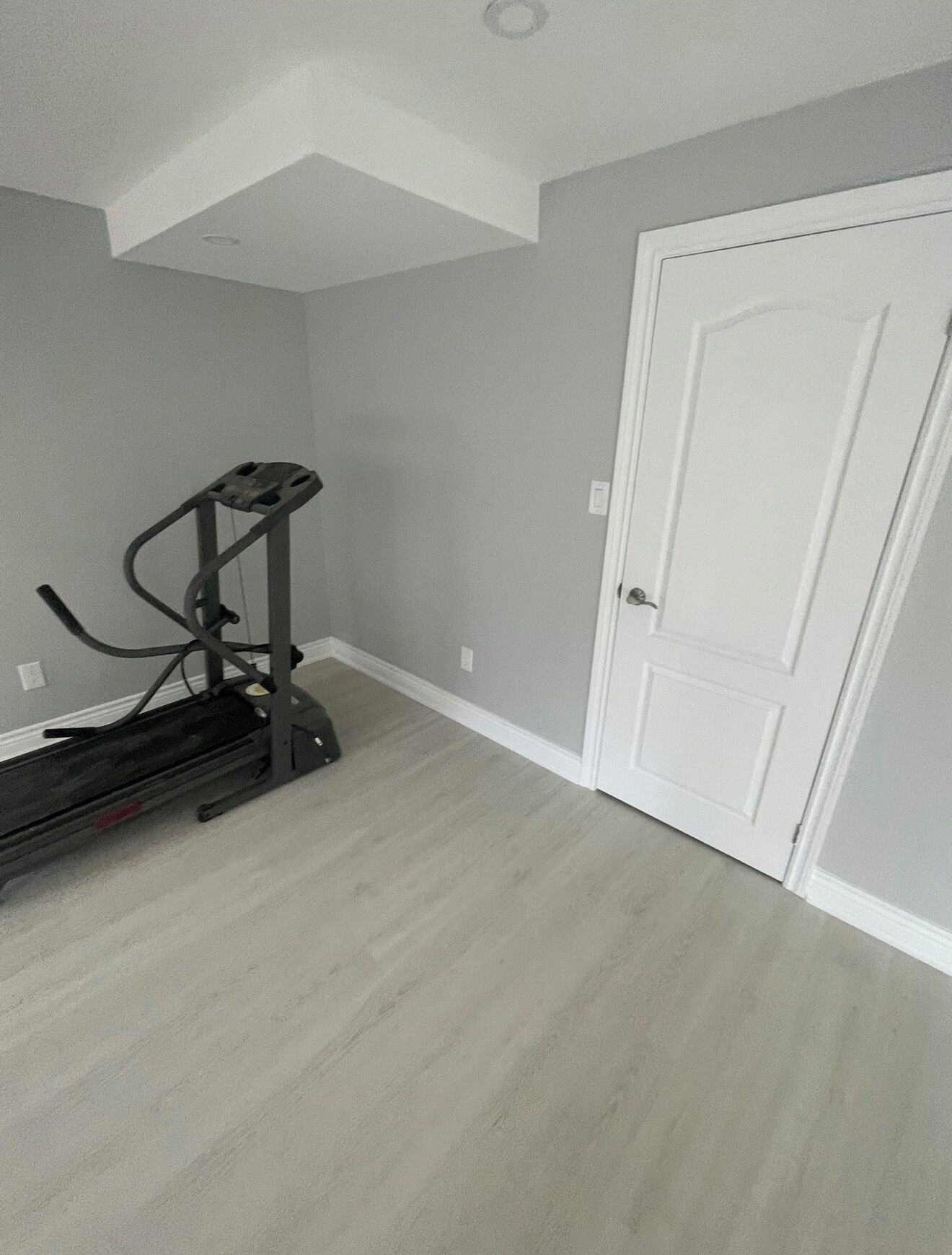A room with a treadmill, a white door, and a light grey wall.