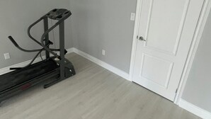 Une pièce avec un tapis de course, une porte blanche et un mur de couleur gris clair.