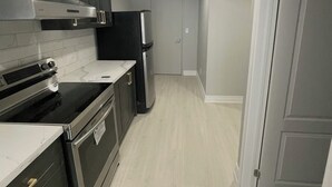 Une cuisine moderne avec des meubles de couleur sombre, des appareils électroménagers en acier inoxydable et un plancher en bois clair.