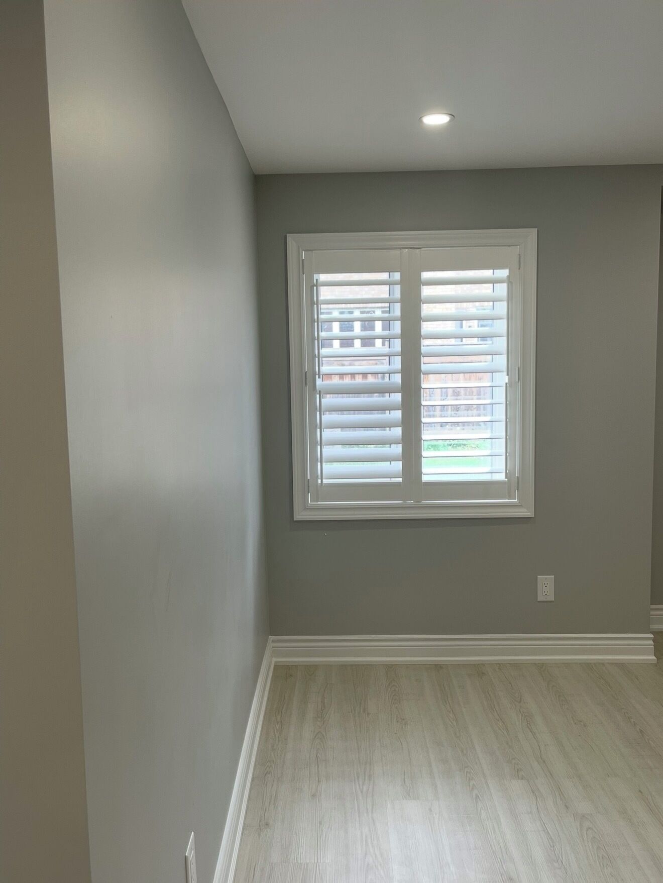 A room with a large window, light grey walls, and a wooden floor.