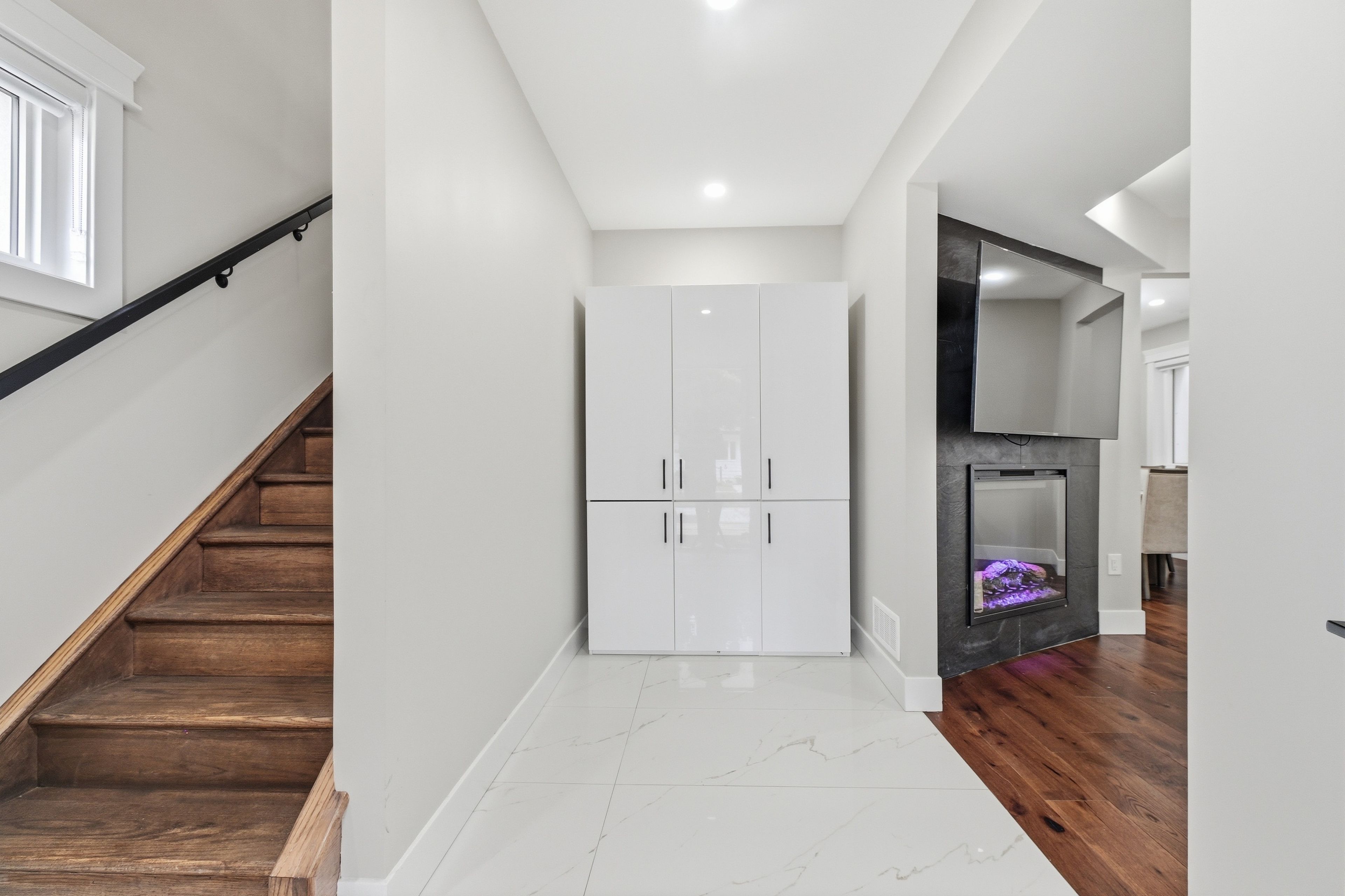 A modern interior with a staircase, a white wardrobe, and a fireplace.