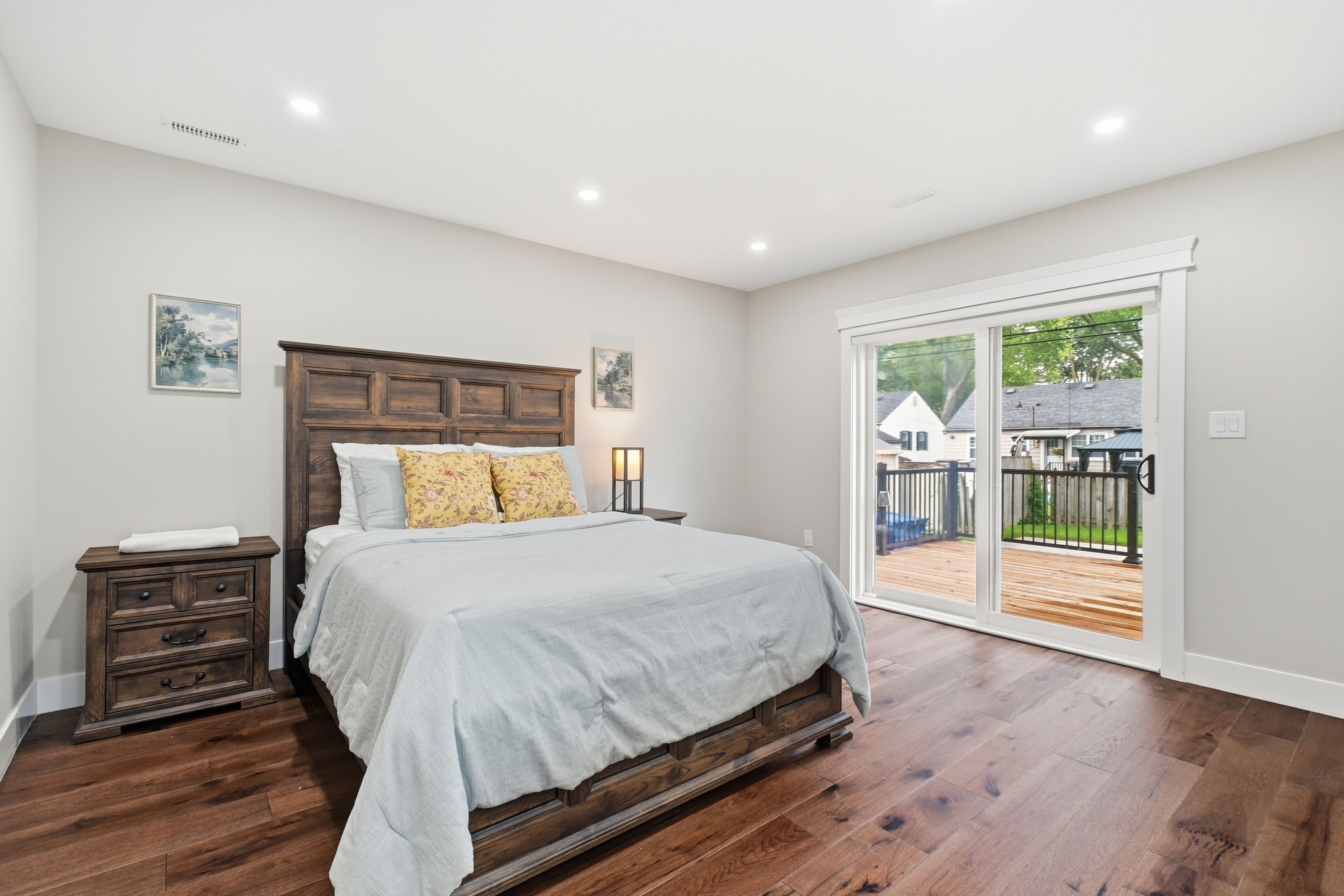 A bedroom with a wooden bed, a nightstand, a dresser, and a sliding glass door leading to an outdoor deck.