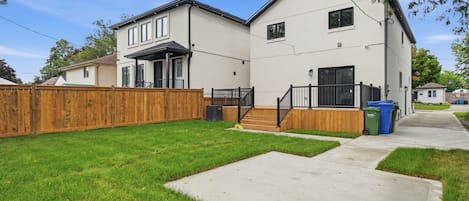 A two-story residential building with a front porch, a wooden fence, and a paved driveway.