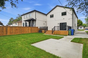 A two-story residential building with a front porch, a wooden fence, and a paved driveway.