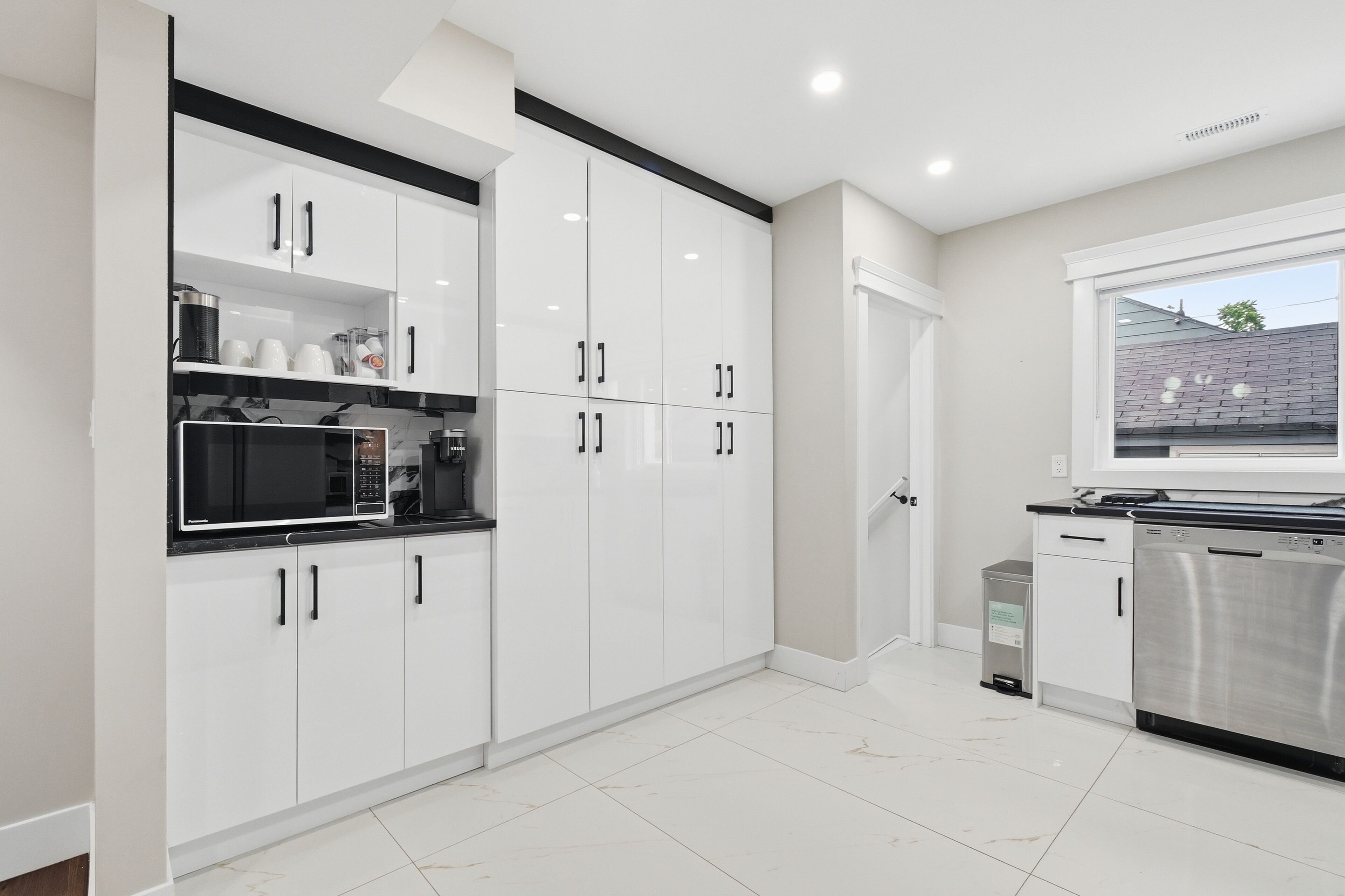 A modern kitchen with white cabinetry, a built-in microwave, and a stainless steel dishwasher.