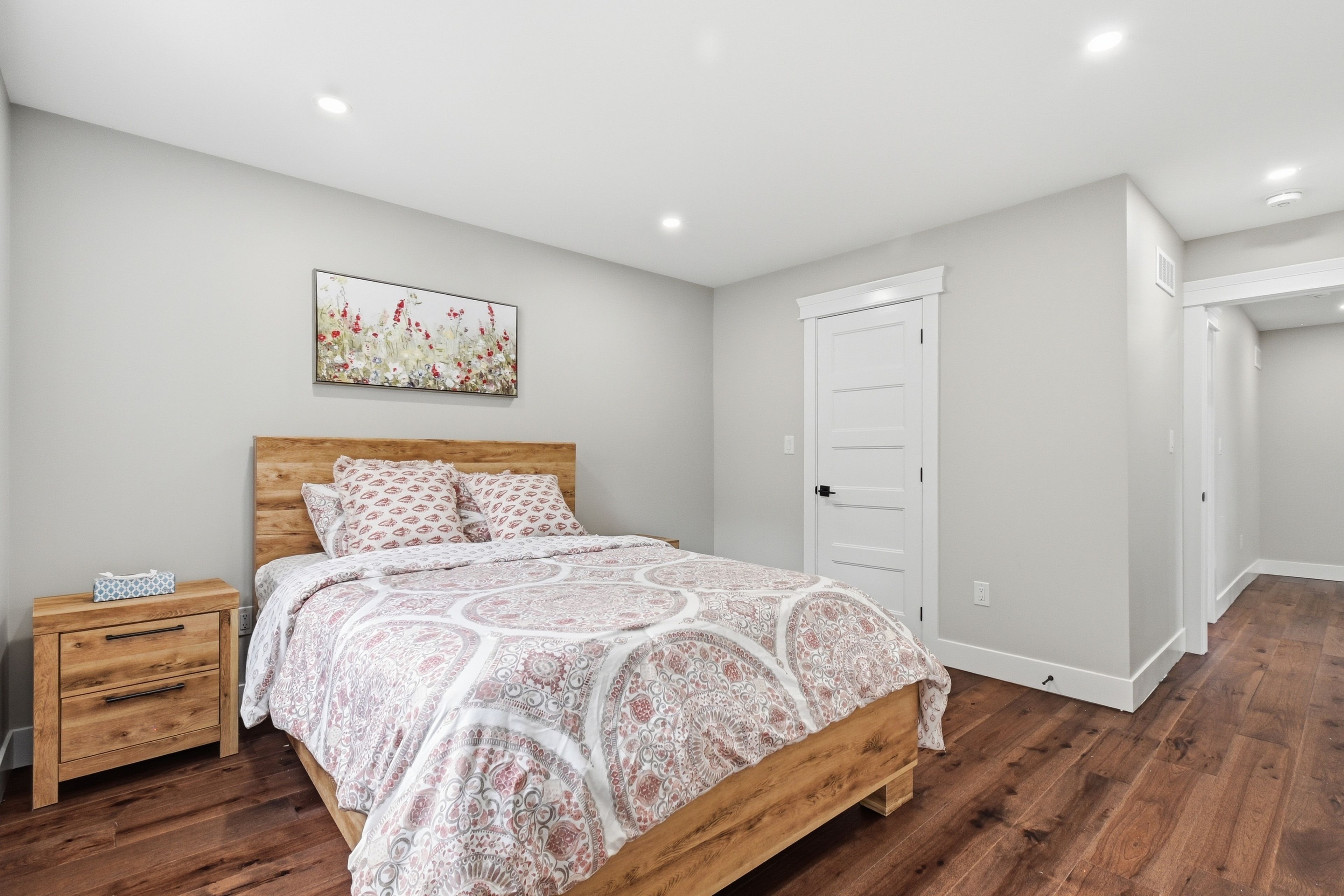 Un dormitorio con cama de madera, una mesita de noche, una puerta blanca y un cuadro colgado en la pared.
