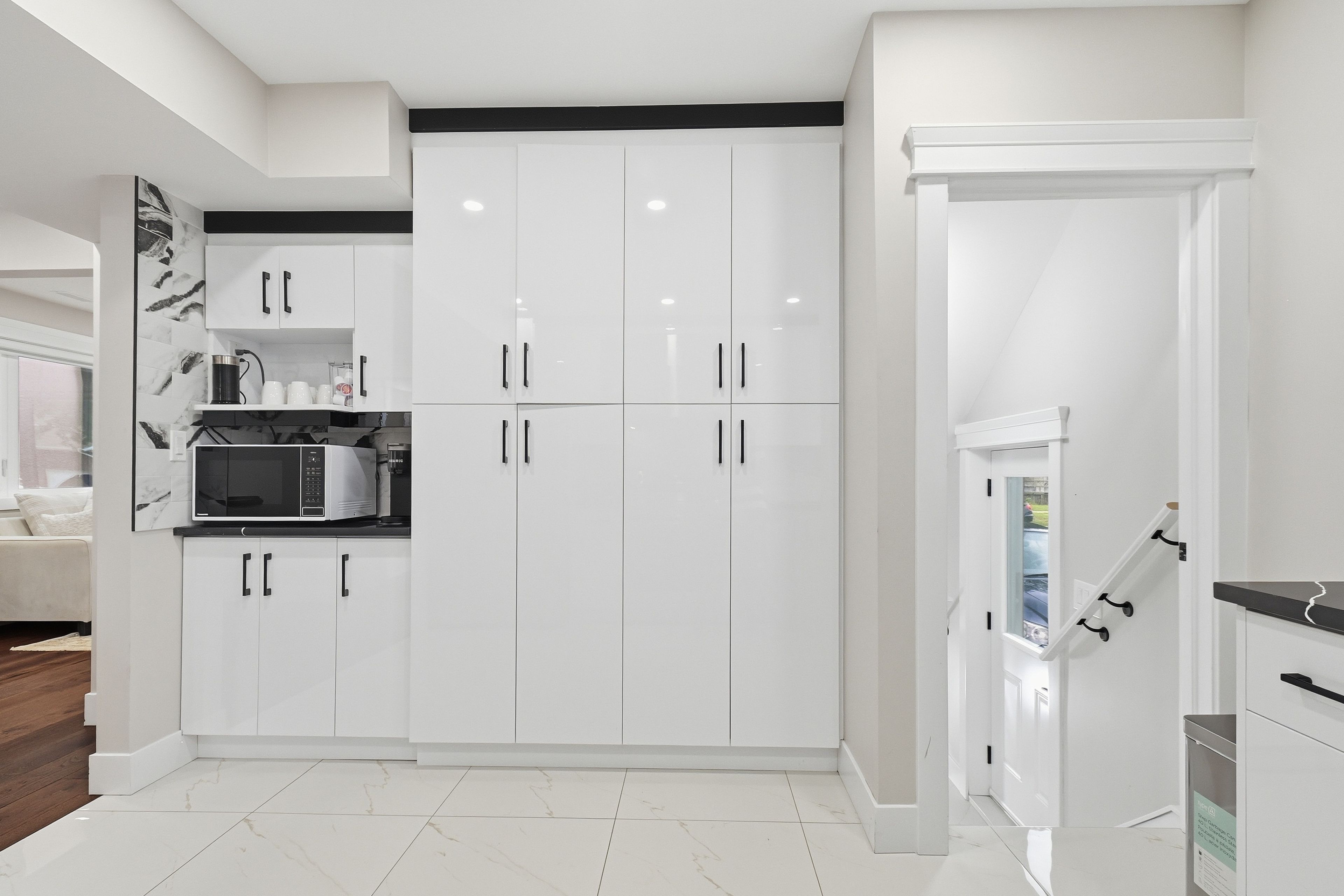 A modern kitchen with white cabinetry, a built-in microwave, and a black countertop.