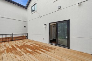 A wooden deck with a black railing, a sliding glass door, and a white exterior wall.