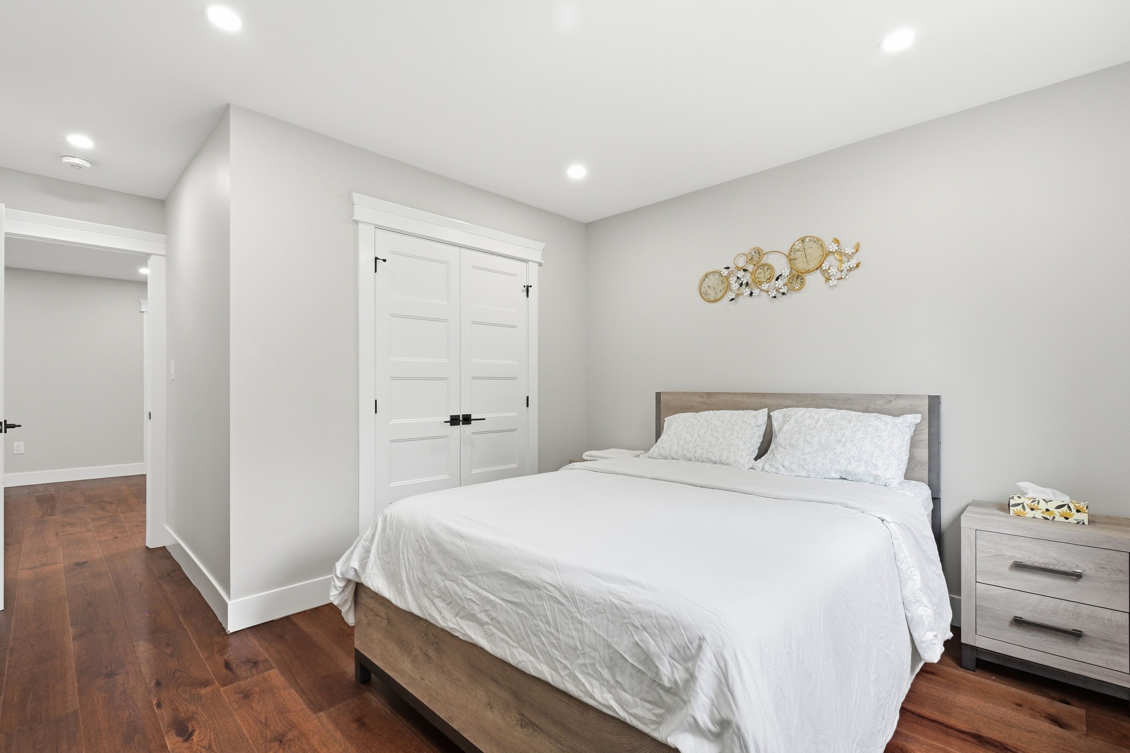 A bedroom with a bed, nightstand, dresser, and a wall clock.