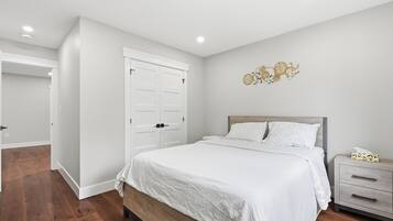 A bedroom with a bed, nightstand, dresser, and a wall clock.