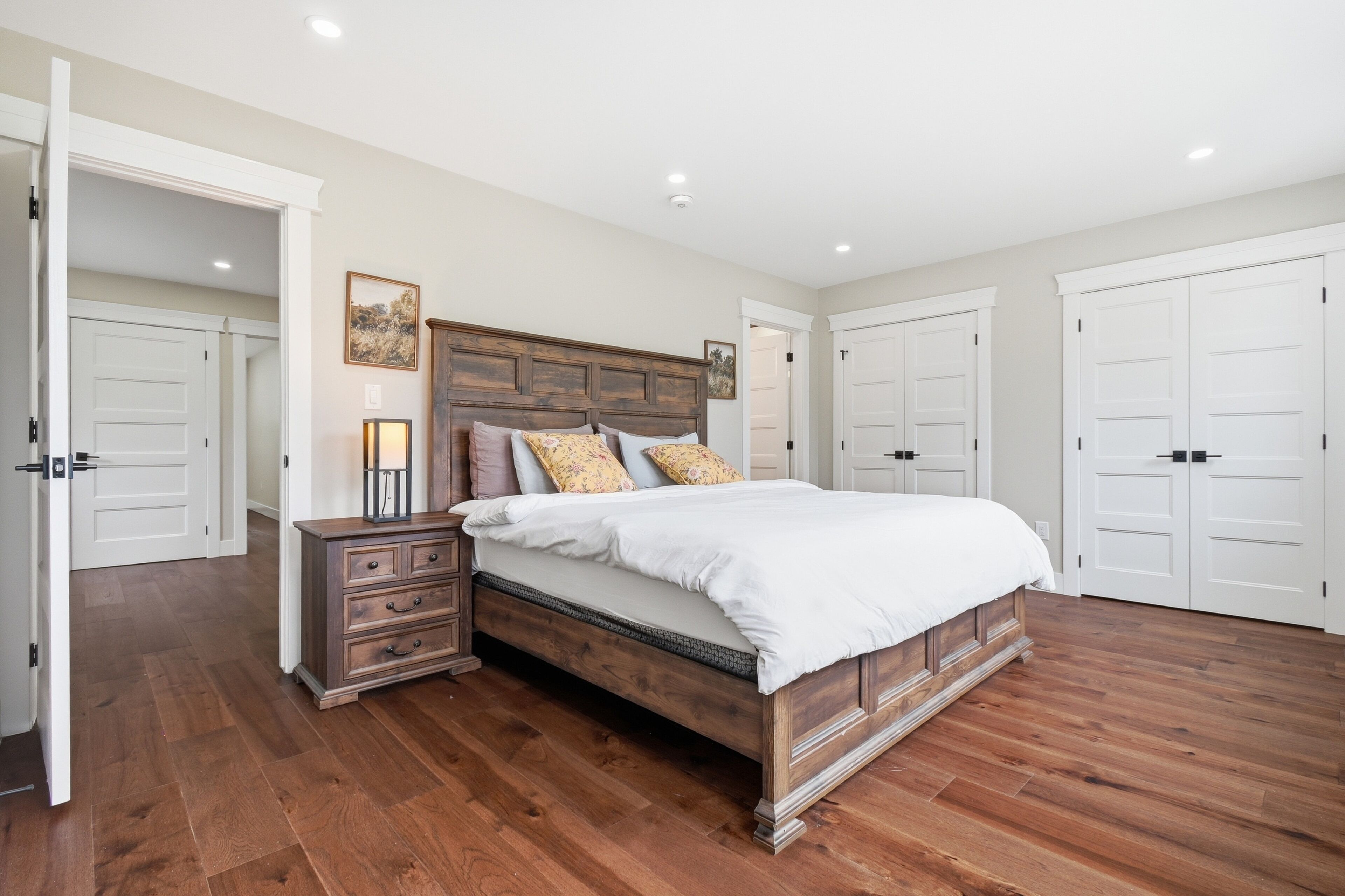 A bedroom with a wooden bed, a nightstand, and a dresser. There are white doors and a hallway visible.