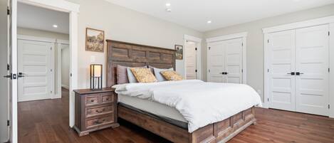 A bedroom with a wooden bed, a nightstand, and a dresser. There are white doors and a hallway visible.