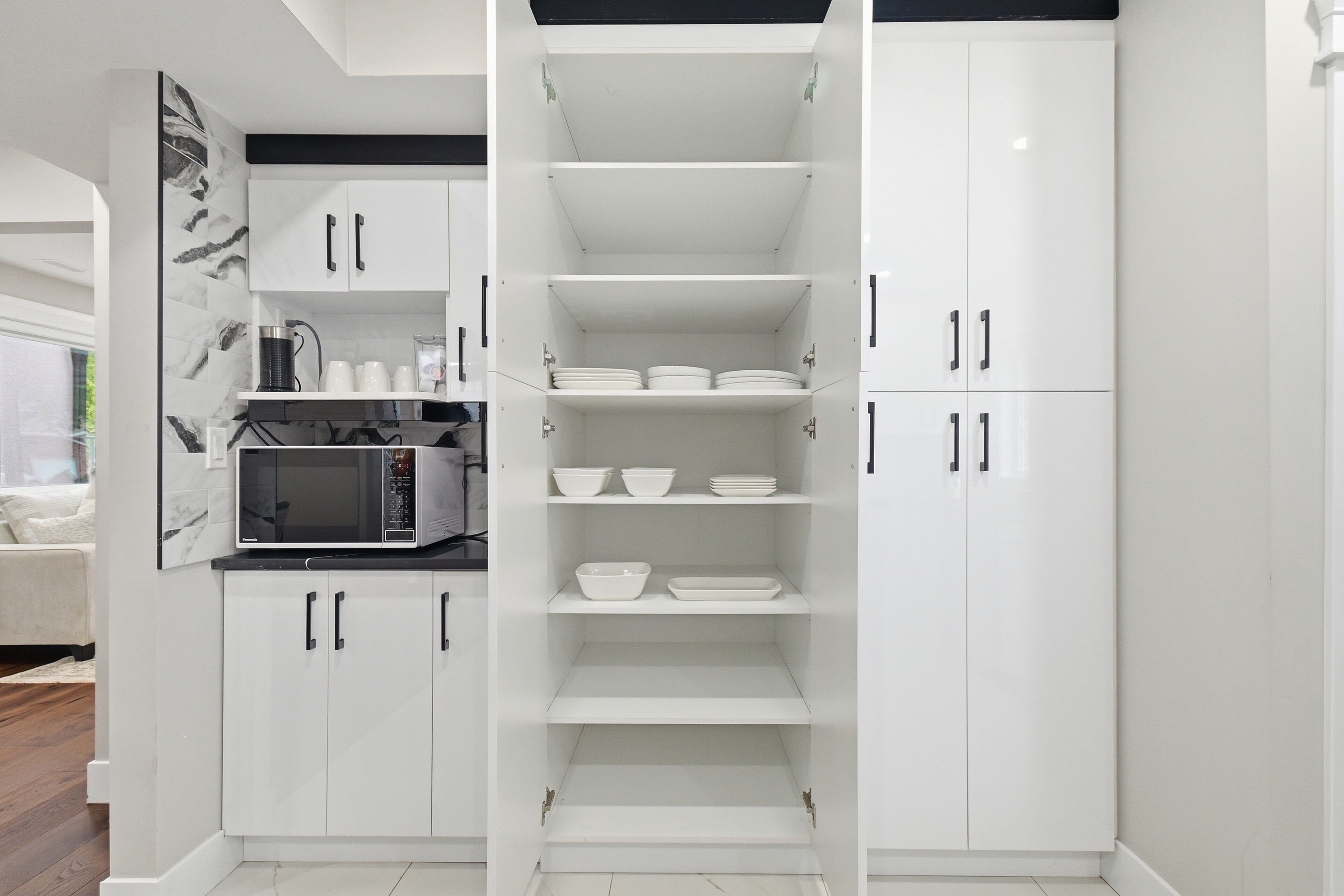 A modern kitchen with white cabinetry, a built-in microwave, and shelves for dishes and utensils.