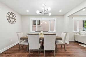 A dining area with a wooden table, six chairs, a wall clock, and a ceiling light fixture. - Premium Windsor Retreat |Perfect for Families, Groups & Long Stays+ Free Parking (Windsor)