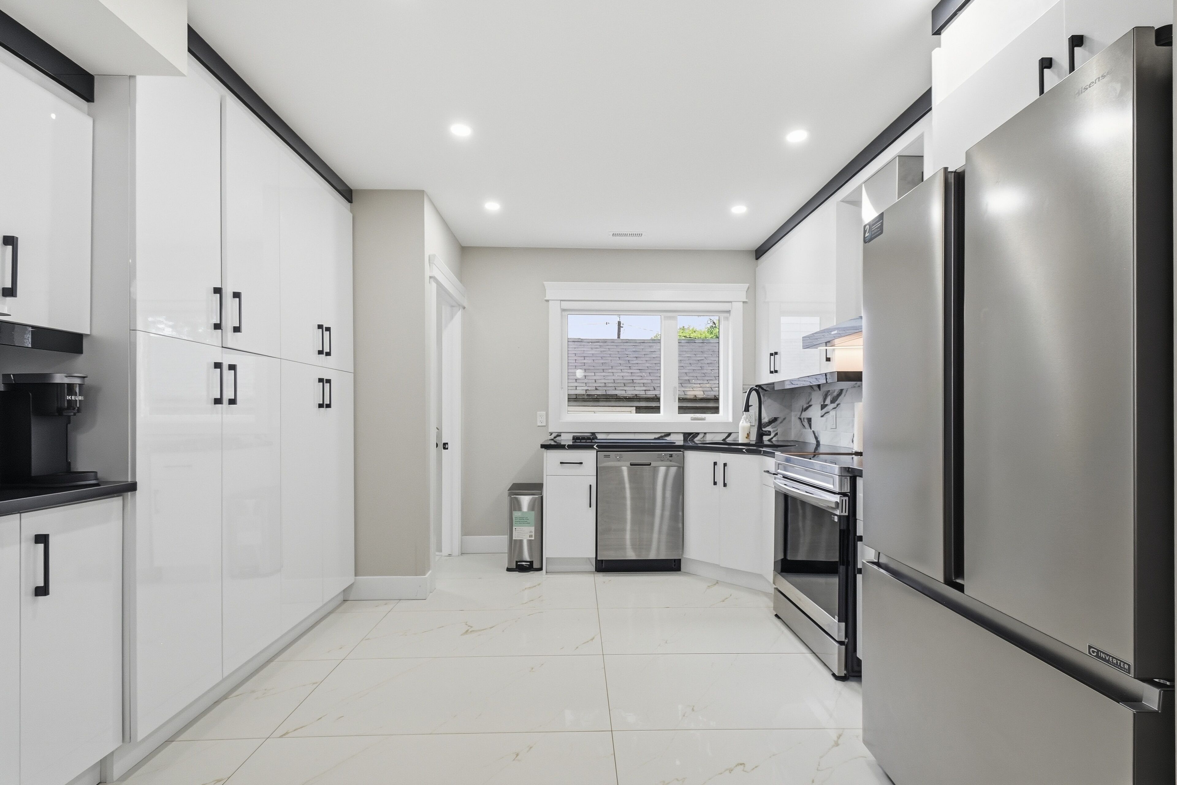 A modern kitchen with white cabinetry, stainless steel appliances, and a tiled floor.