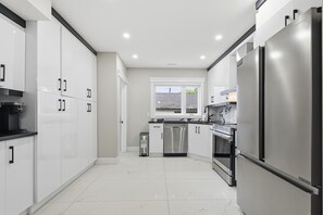 A modern kitchen with white cabinetry, stainless steel appliances, and a tiled floor. - New 4BR |Main Floor -Ensuite |Group & Family |Free Parking | Weekend & Long-Stay (Windsor)