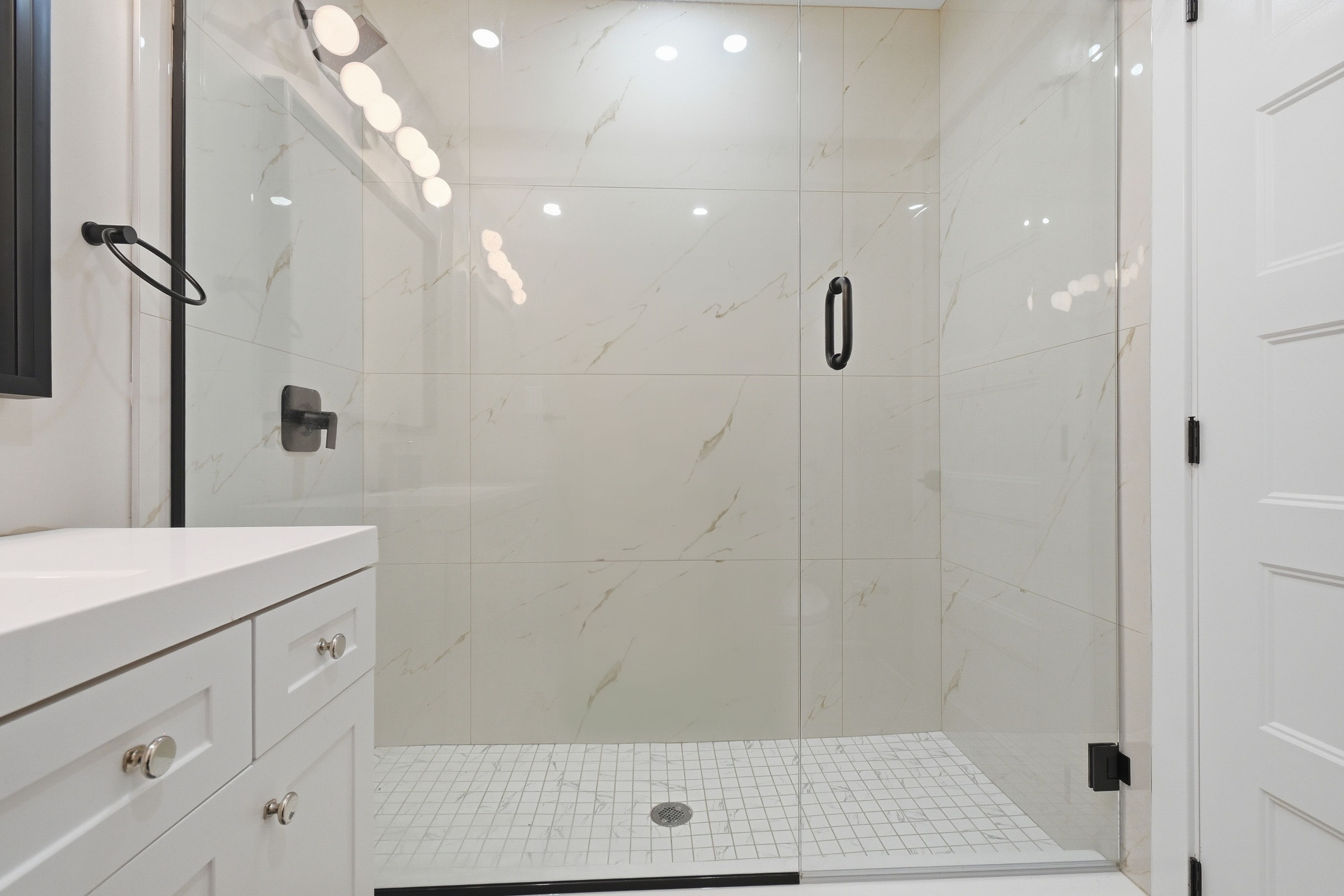 Een moderne badkamer met een witte marmeren wand, een douchecabine van glas en een wit badmeubel met lades.