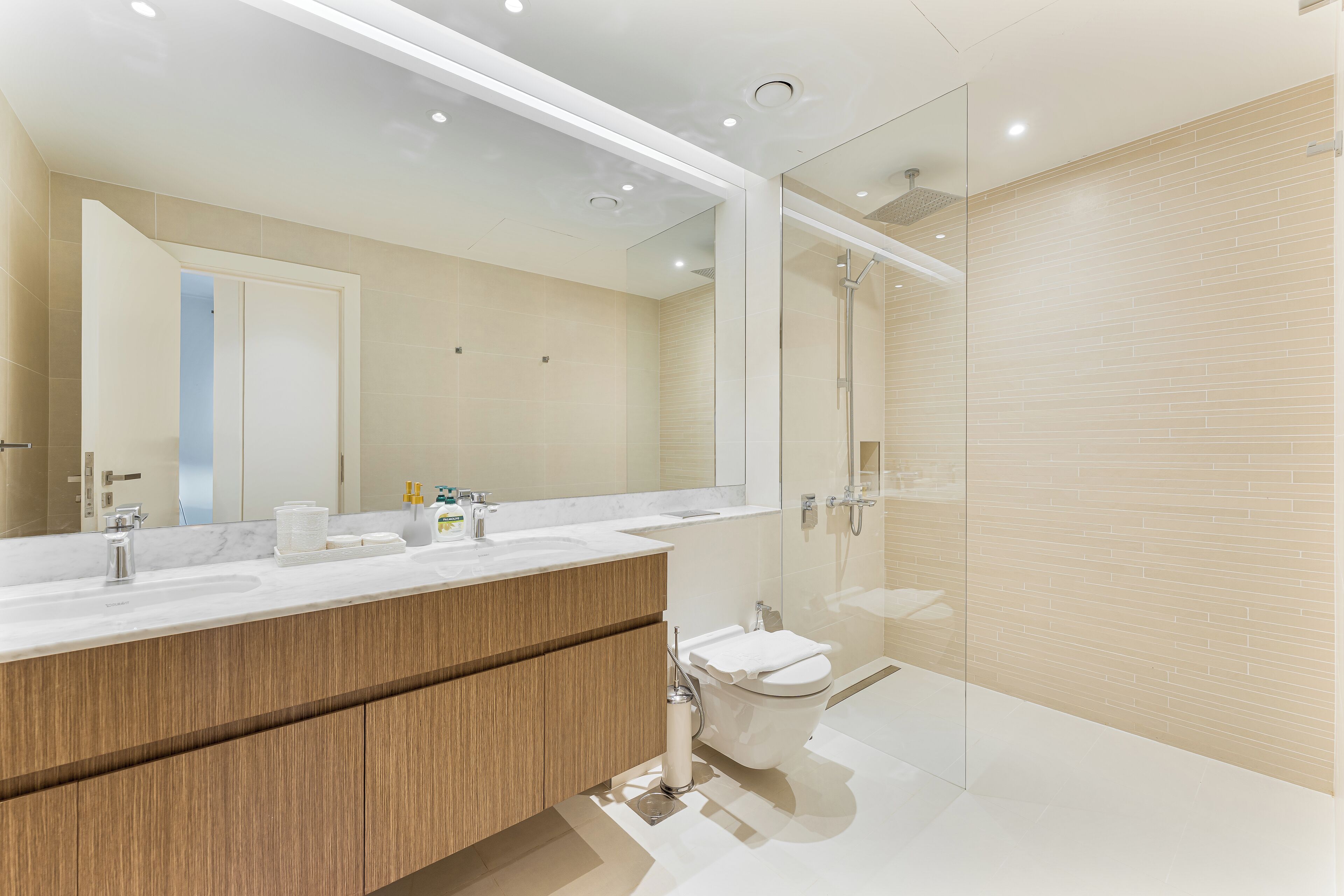 A modern bathroom with a large mirror, a shower, and a toilet.