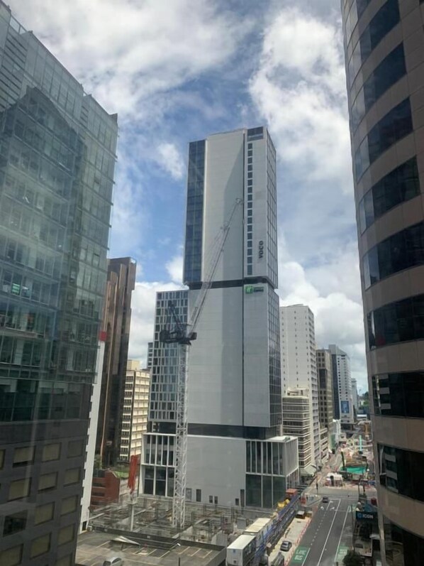 A modern high-rise building with a prominent corner structure, surrounded by other tall buildings. - Garden Hostel (Auckland)