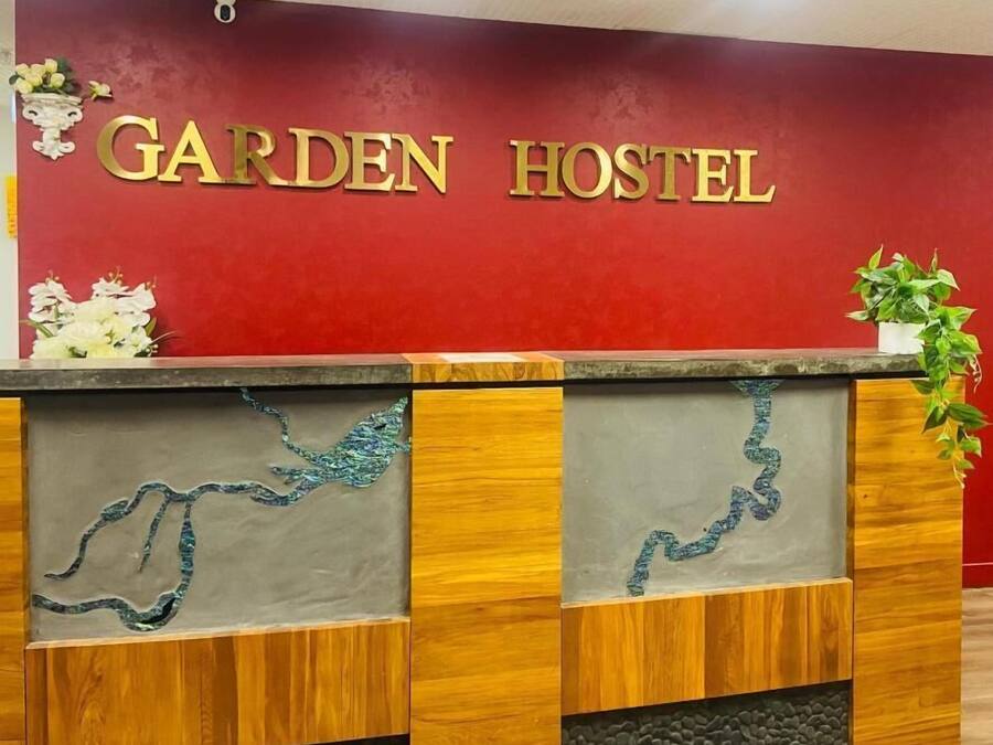 Un mostrador de recepción con pared roja y las palabras 'GARDEN HOSTEL' en letras doradas.