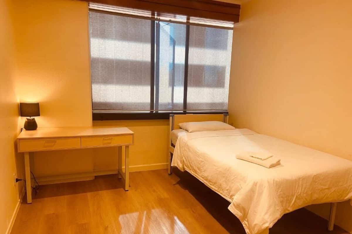 Une chambre avec un lit, un bureau et une fenêtre avec des stores.