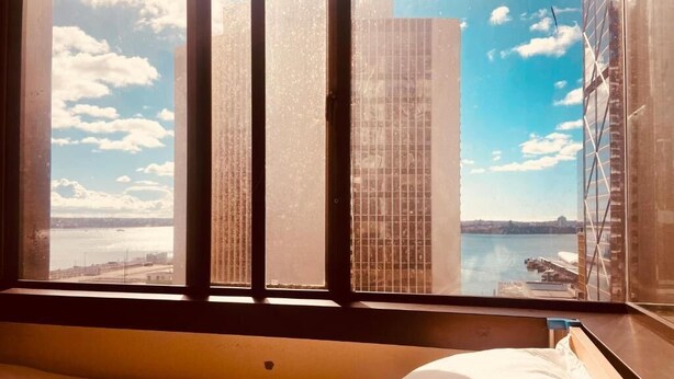 A room with a large window, a bed, and a view of a cityscape and water. - Garden Hostel (Auckland)