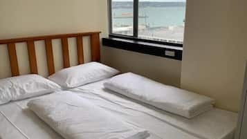 Una cama con sábanas blancas, cabecera de madera y ventana con vista al mar y un puente.