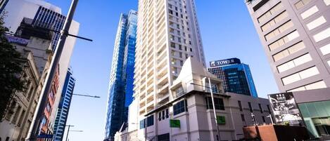 A cityscape with modern high-rise buildings, a street with cars, and a clear blue sky.