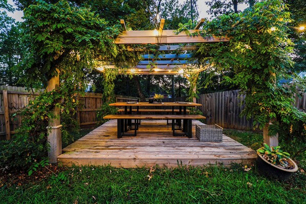 Une terrasse en bois avec une table de pique-nique et des bancs, entourée d’une clôture en bois et de verdure.