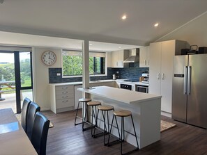 A modern kitchen with a central island, bar stools, a stainless steel refrigerator, and a view of the outdoors.