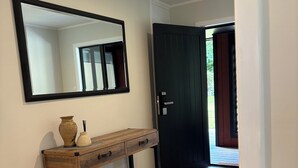 Un couloir avec une console en bois, un grand miroir, une porte sombre et un tapis à motifs.