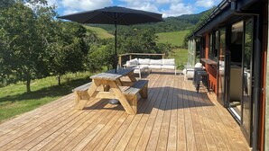 Une terrasse en bois aménagée avec du mobilier d’extérieur, notamment une table, des chaises et un parasol.