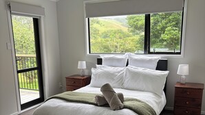 Une chambre dotée d’un grand lit, de deux tables de chevet, d’une fenêtre donnant sur un espace verdoyant et d’une porte coulissante menant à un balcon.