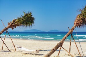 A beach with palm trees, a hammock, and a clear view of the ocean and distant mountains.