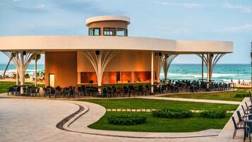 A modern building with a curved roof, outdoor seating, and a view of the ocean.
