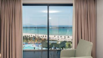 A room with a large sliding glass door leading to a balcony with a view of a beach and resort.