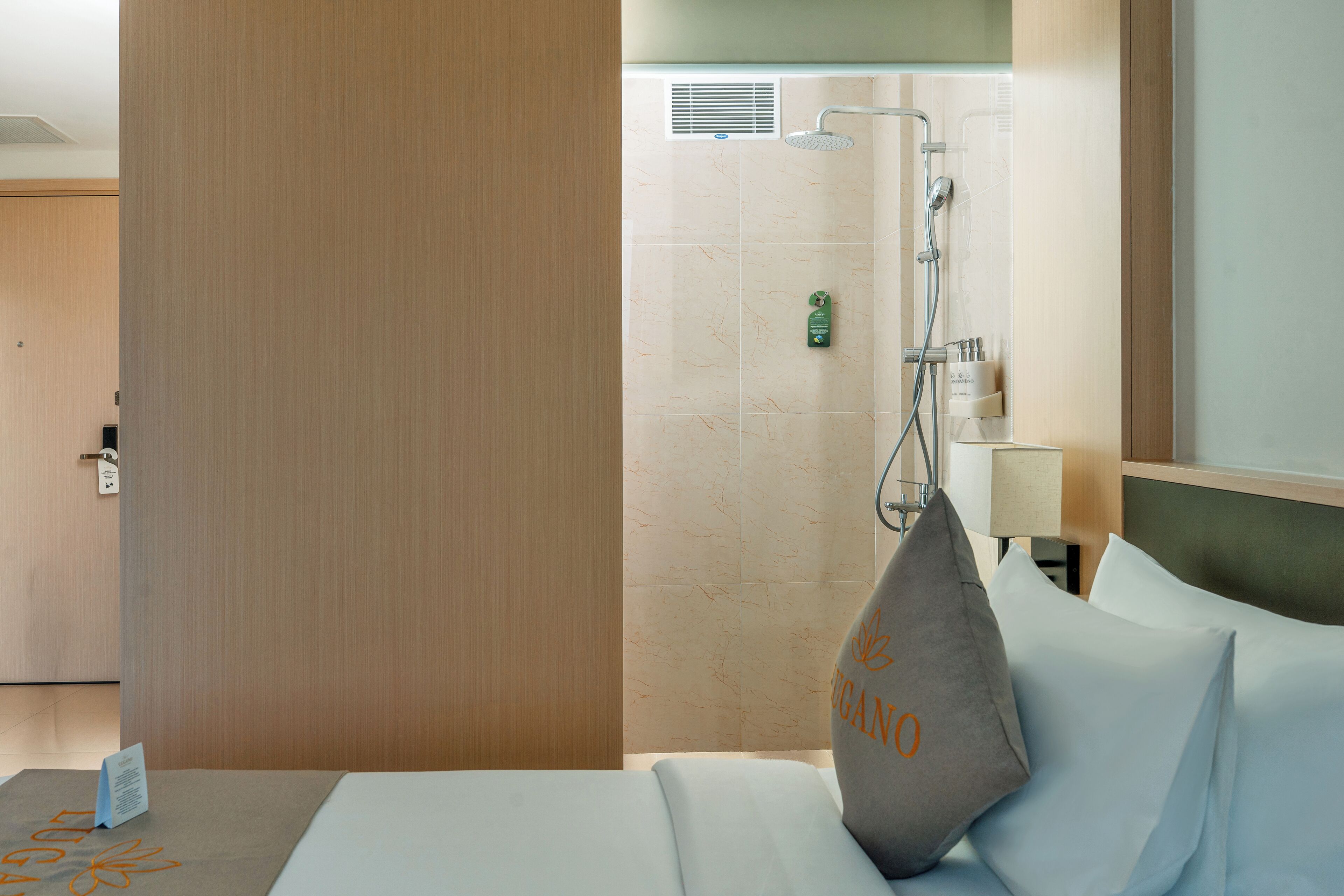 A hotel room with a bed, pillows, a nightstand, a lamp, and a shower area.