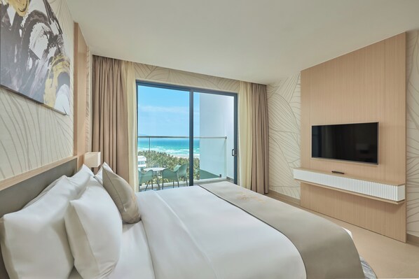 Habitación de hotel con una cama grande, un televisor montado en la pared y un balcón con vista al océano.