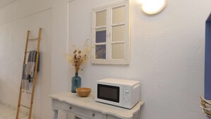Eine weiße Mikrowelle auf einem weißen Tisch, darüber ein Fenster, eine Holzleiter und eine Vase mit getrockneten Blumen.