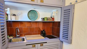 Eine kleine Küche mit Spüle, Wasserhahn und Schneidebrett auf der Arbeitsfläche.