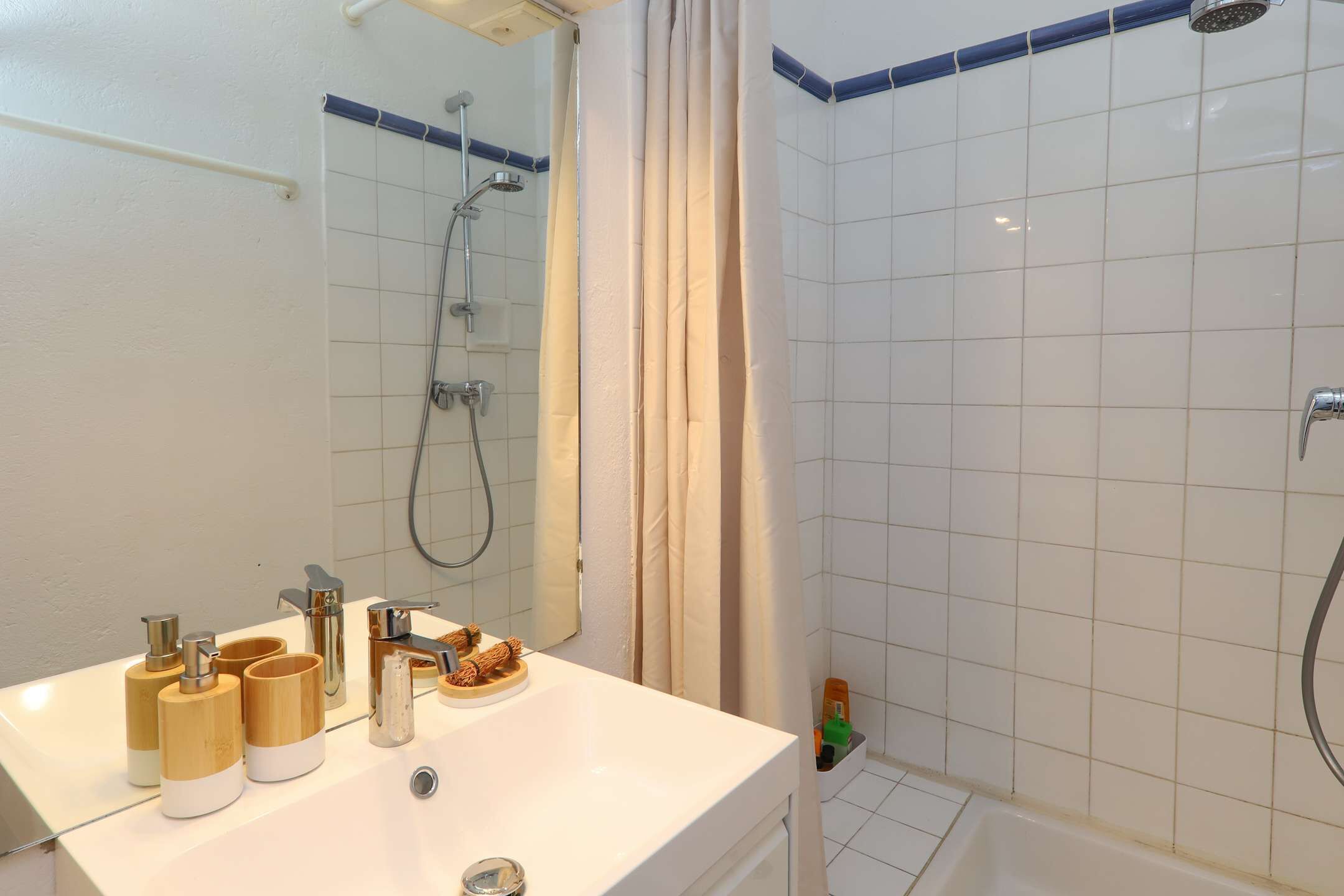 Une salle de bain avec un lavabo blanc, des articles de toilette en bois, une douche et une baignoire.