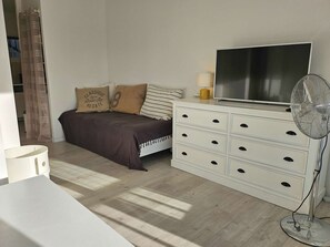 A bedroom with a bed, a dresser, a TV, and a standing fan. - Luminous, air-conditioned studio with canal views, close to the beach. (PORT GRIMAUD)
