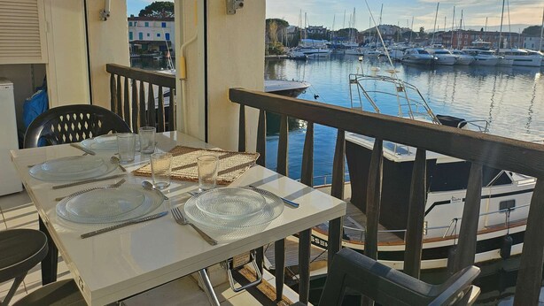 Et spisebord dækket med tallerkener, bestik og glas på en balkon med udsigt over en havn med både.
